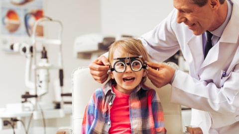 Enfant souriante essayant des lunettes, accompagnée d’un praticien